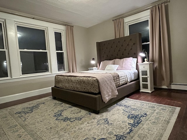 bedroom with dark wood finished floors, a baseboard heating unit, and baseboards