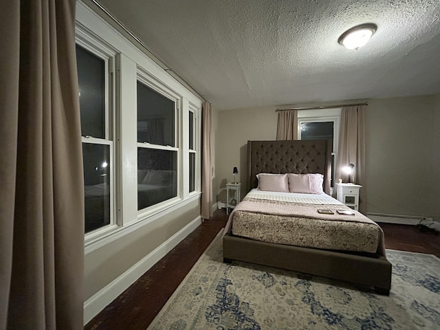 bedroom with a baseboard heating unit, a textured ceiling, baseboards, and dark wood-style floors