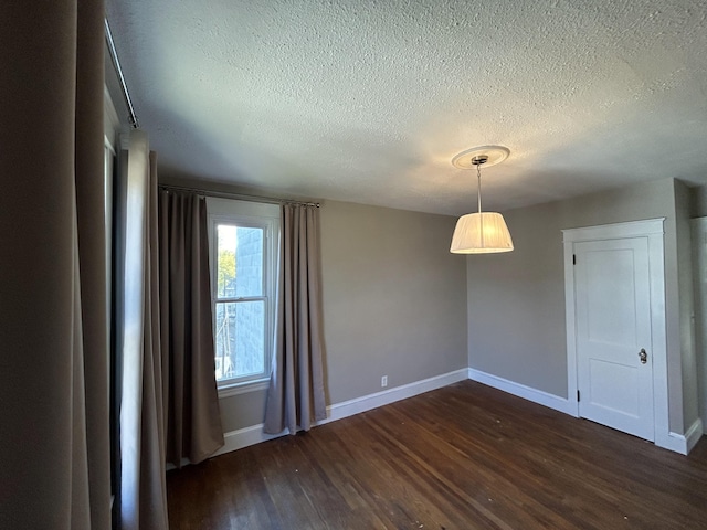 spare room with a textured ceiling, dark wood-style floors, and baseboards