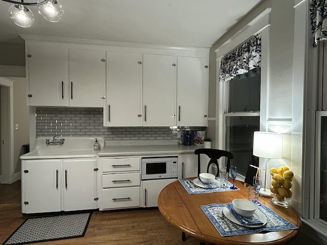 kitchen featuring white microwave, backsplash, light countertops, a sink, and white cabinetry