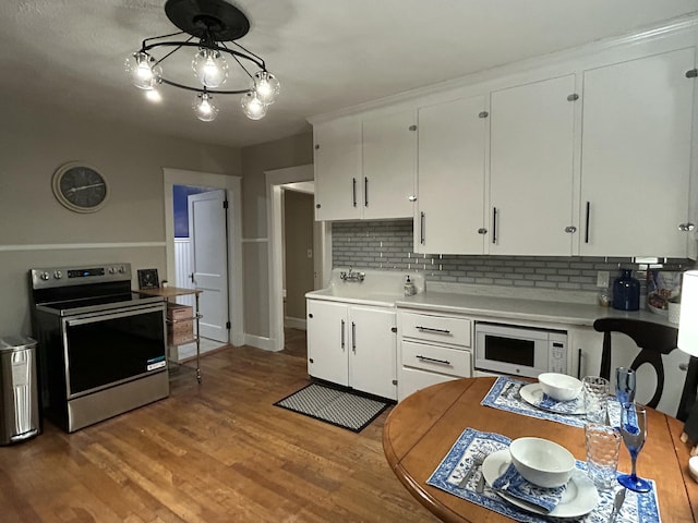 kitchen featuring electric range, white microwave, light countertops, backsplash, and white cabinetry