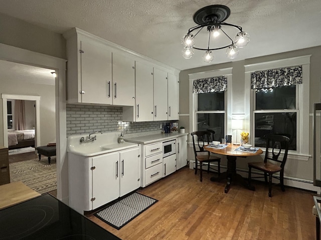 kitchen with light countertops, white cabinetry, decorative backsplash, white microwave, and wood finished floors
