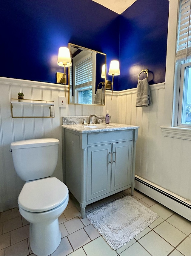 bathroom with a wainscoted wall, a baseboard heating unit, toilet, tile patterned floors, and vanity