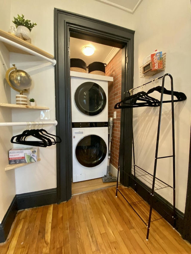 laundry area with stacked washer / dryer, ornamental molding, hardwood / wood-style flooring, and baseboards