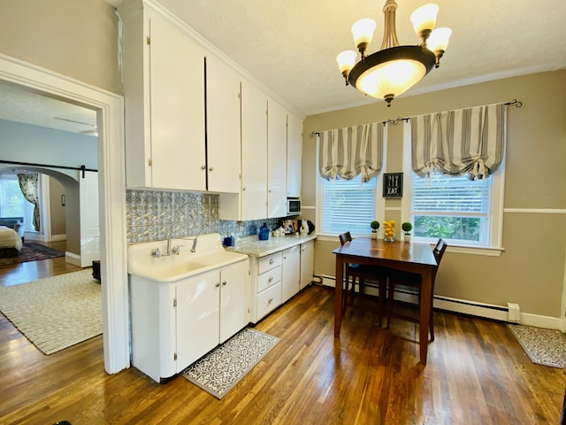 kitchen featuring arched walkways, light countertops, wood finished floors, decorative backsplash, and white cabinets