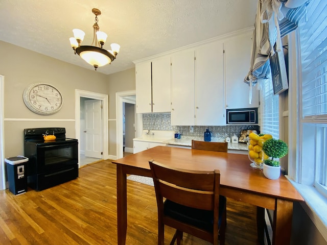kitchen with black electric range, white cabinets, wood finished floors, a chandelier, and light countertops