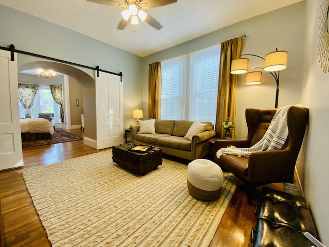 living room with a barn door, arched walkways, a ceiling fan, and wood finished floors