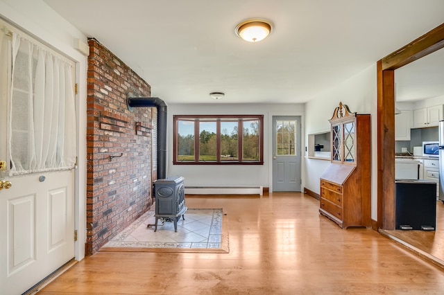 entrance foyer featuring a baseboard radiator, a wood stove, light wood-type flooring, brick wall, and baseboards