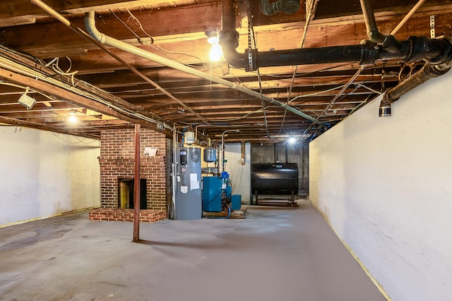 unfinished basement featuring oil tank, heat pump water heater, a heating unit, and a brick fireplace