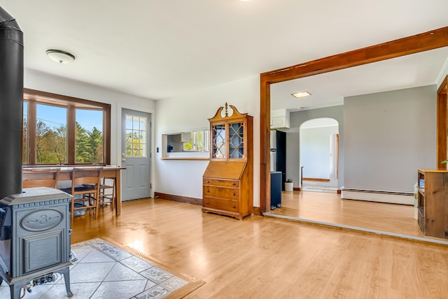 office with a wood stove, arched walkways, baseboard heating, light wood-type flooring, and baseboards