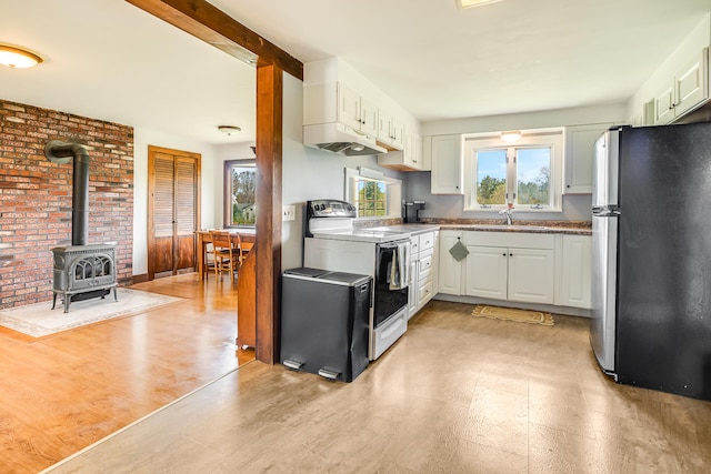 kitchen featuring freestanding refrigerator, electric range, a wood stove, white cabinets, and under cabinet range hood