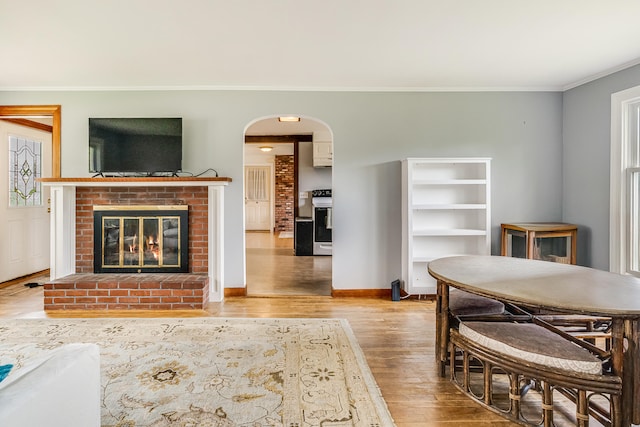 living area with wood finished floors, crown molding, arched walkways, a fireplace, and baseboards