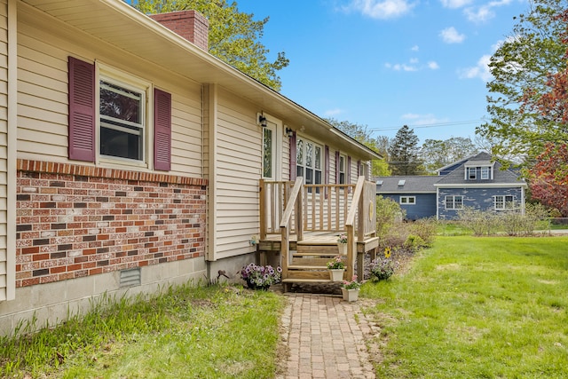property entrance featuring a chimney, a lawn, and brick siding
