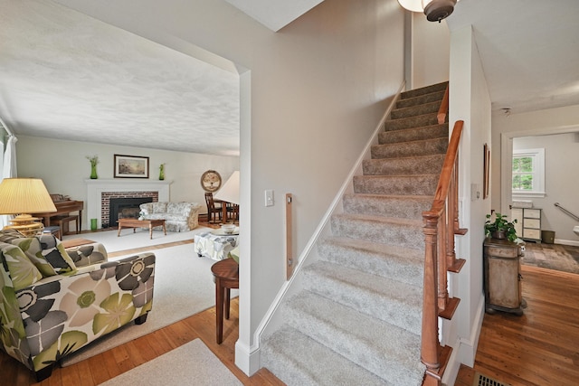 staircase with wood finished floors and a brick fireplace