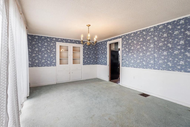 carpeted spare room featuring wainscoting, a chandelier, ornamental molding, wallpapered walls, and a textured ceiling