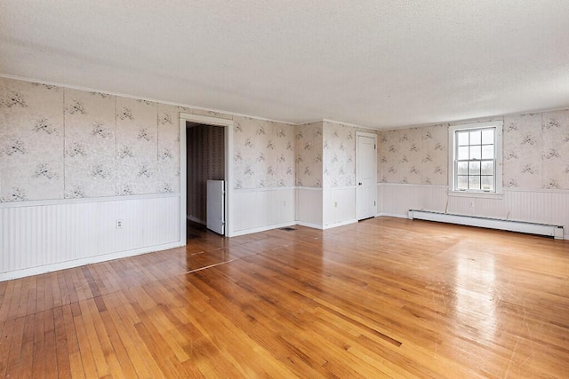 spare room with a baseboard radiator, wainscoting, hardwood / wood-style floors, and wallpapered walls