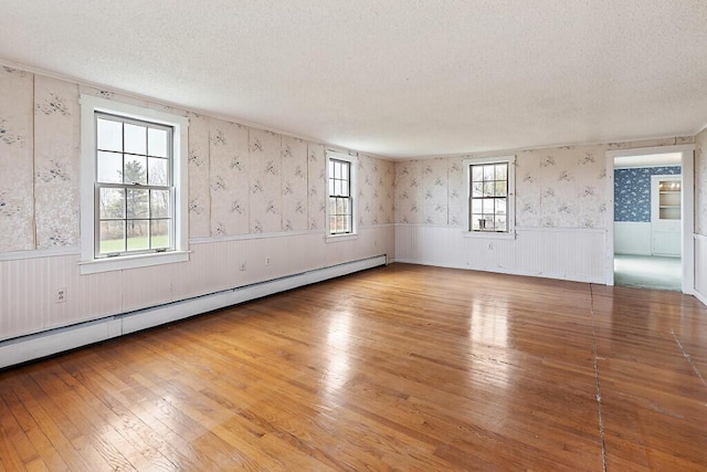 unfurnished room with a textured ceiling, a wainscoted wall, a baseboard radiator, wood-type flooring, and wallpapered walls