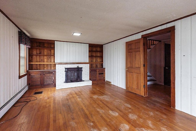 unfurnished living room with a baseboard heating unit, hardwood / wood-style floors, a textured ceiling, built in shelves, and crown molding