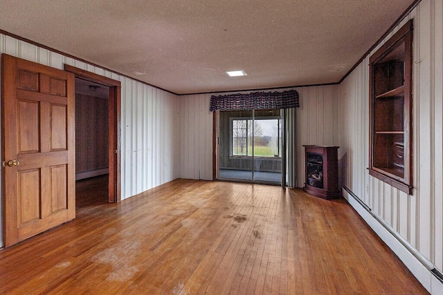 unfurnished living room with a baseboard heating unit, ornamental molding, a textured ceiling, light wood-type flooring, and a fireplace