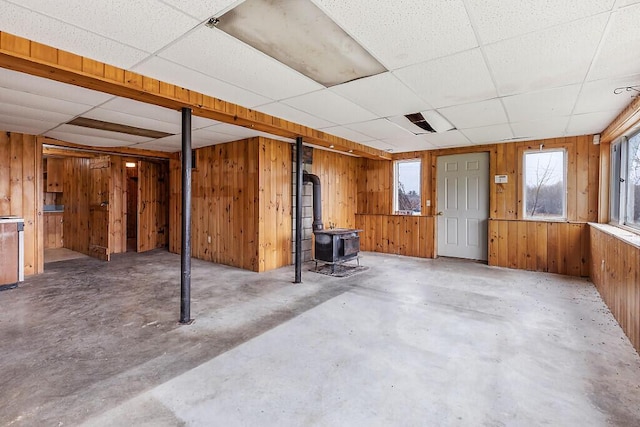 basement with a drop ceiling, a wood stove, wood walls, and healthy amount of natural light