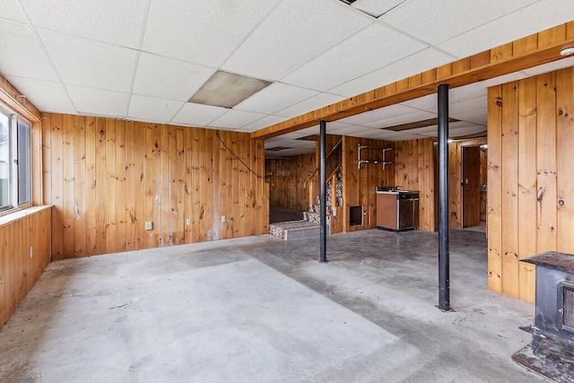 below grade area with a drop ceiling, wooden walls, and stairway