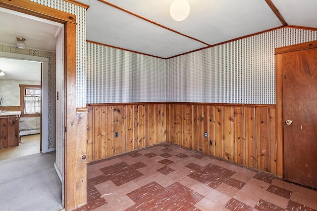 spare room featuring baseboard heating, tile patterned floors, a wainscoted wall, crown molding, and vaulted ceiling