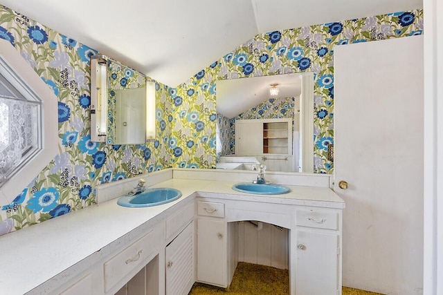 bathroom featuring wallpapered walls, lofted ceiling, and double vanity