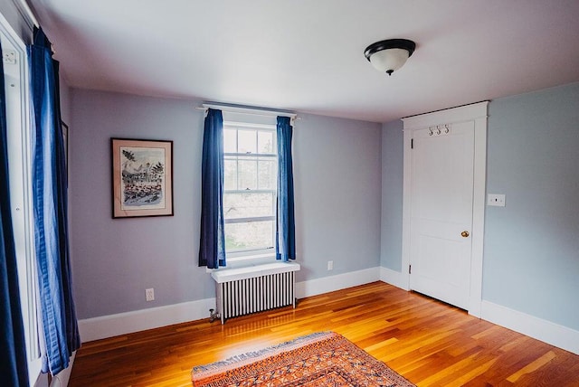 unfurnished room featuring radiator, light wood-style floors, and baseboards