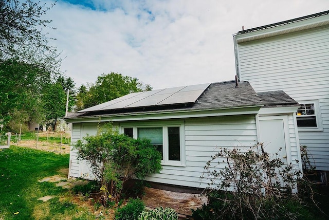 view of side of home with solar panels, roof with shingles, and a yard