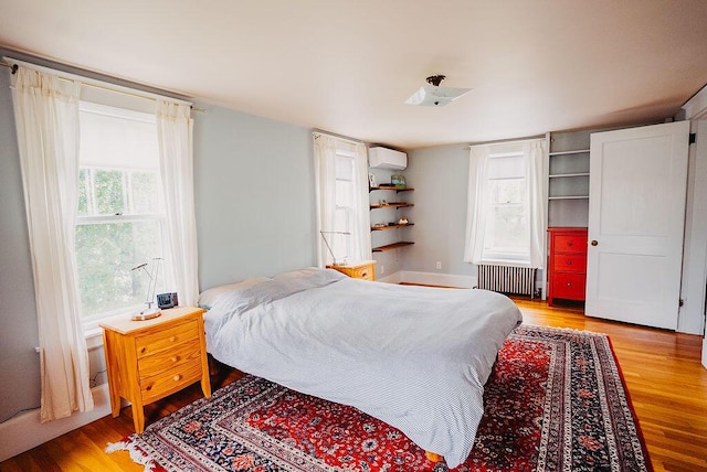 bedroom with radiator heating unit, a wall unit AC, and light wood-style flooring