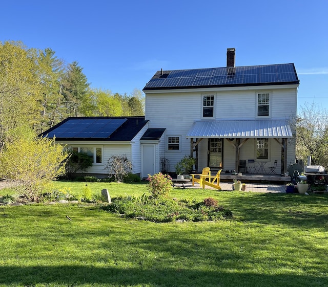 back of house with solar panels, a chimney, a yard, and metal roof