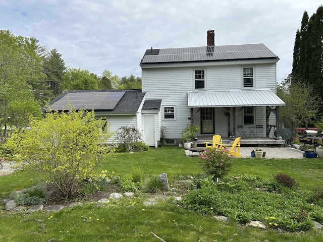 rear view of house with solar panels, a chimney, a lawn, and metal roof