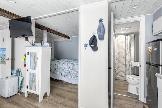 bedroom with wood finished floors, wood ceiling, connected bathroom, and freestanding refrigerator