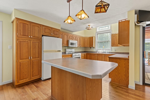 kitchen featuring white appliances, light wood finished floors, decorative light fixtures, brown cabinets, and a center island
