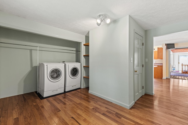 clothes washing area with washer and clothes dryer, wood finished floors, and a textured ceiling