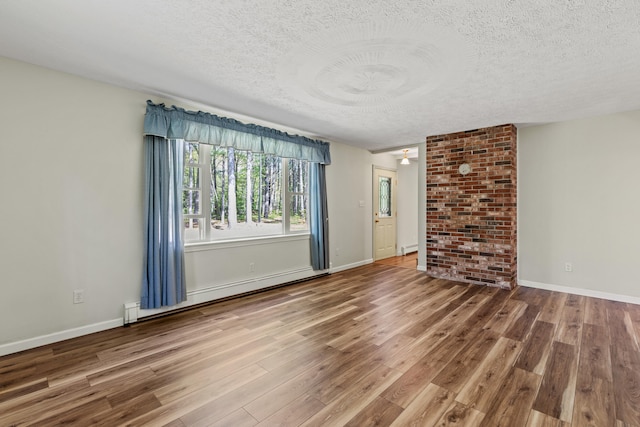 unfurnished living room featuring a textured ceiling, baseboard heating, wood finished floors, and baseboards