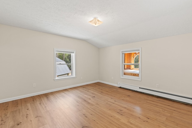 empty room with a baseboard heating unit, lofted ceiling, light wood-style flooring, baseboards, and a textured ceiling