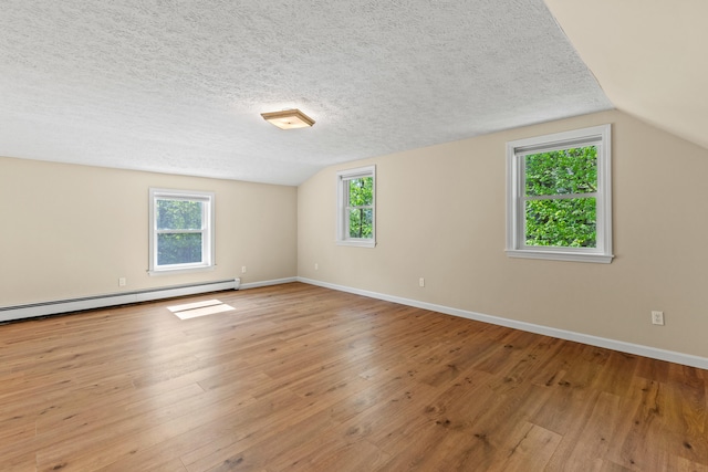 empty room with lofted ceiling, plenty of natural light, wood finished floors, a baseboard heating unit, and baseboards