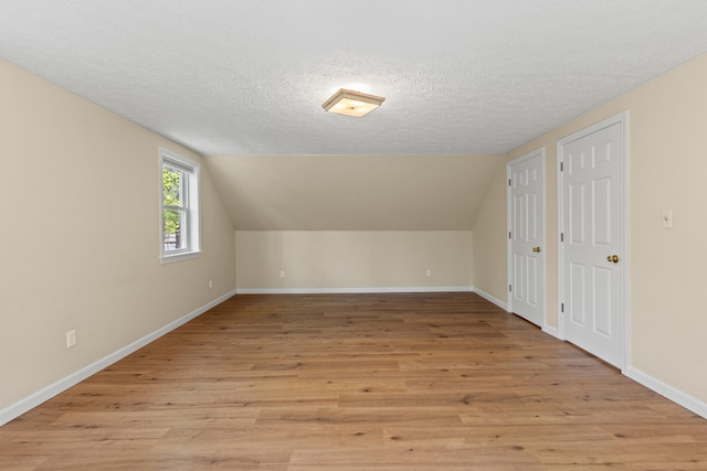 additional living space with a textured ceiling, light wood-style flooring, baseboards, and vaulted ceiling