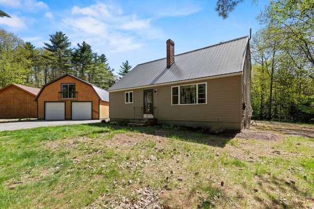colonial inspired home featuring a garage, a chimney, an outbuilding, metal roof, and a front yard