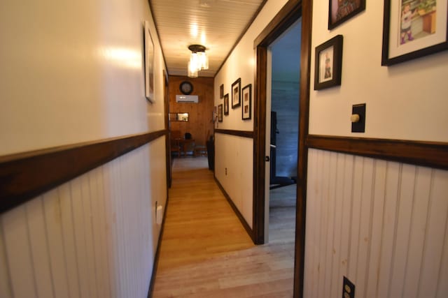 hall featuring light wood-type flooring, wooden walls, and wainscoting