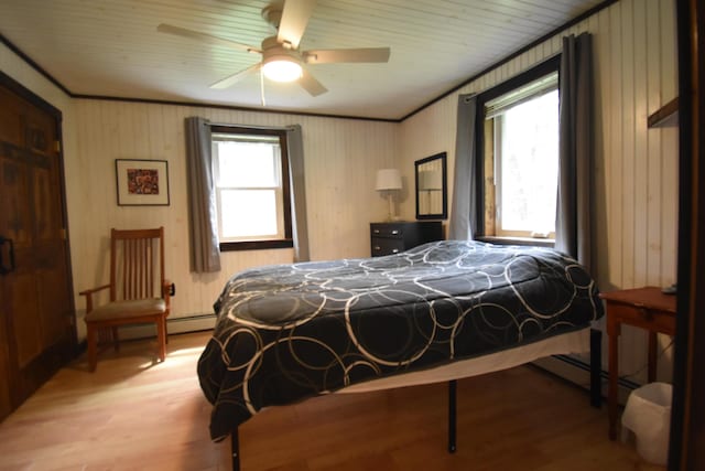bedroom with light wood-style floors, baseboard heating, ceiling fan, and wooden walls