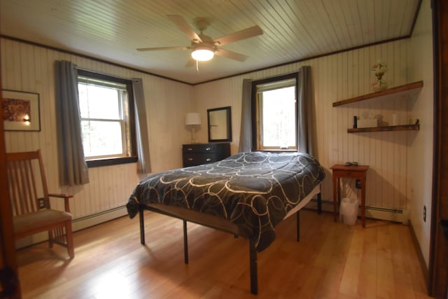 bedroom featuring wood finished floors, multiple windows, a baseboard heating unit, wooden walls, and ceiling fan
