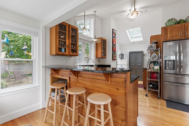 23 Amerescoggin Rd, Falmouth, ME 04105 - kitchen with stainless steel refrigerator with ice dispenser, a skylight, brown cabinetry, stacked washer and clothes dryer, and light wood-style flooring