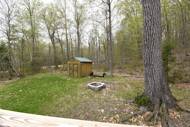 106 Shady Ln, Newport, ME 04953 - view of grassy yard featuring an outdoor fire pit, a storage unit, an outdoor structure, and a wooded view