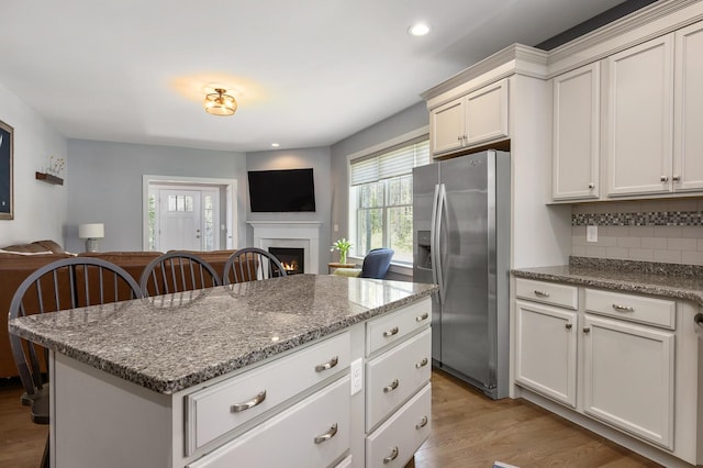 53 Ross Rd, Kennebunk, ME 04043 - kitchen featuring stainless steel refrigerator with ice dispenser, open floor plan, light wood finished floors, decorative backsplash, and a lit fireplace