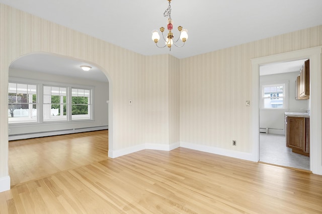 606 Main St, Sanford, ME 04083 - empty room featuring baseboard heating, wallpapered walls, light wood-style floors, arched walkways, and a chandelier