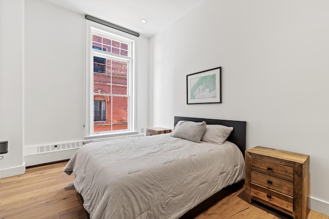 bedroom featuring hardwood / wood-style floors, multiple windows, radiator, and recessed lighting