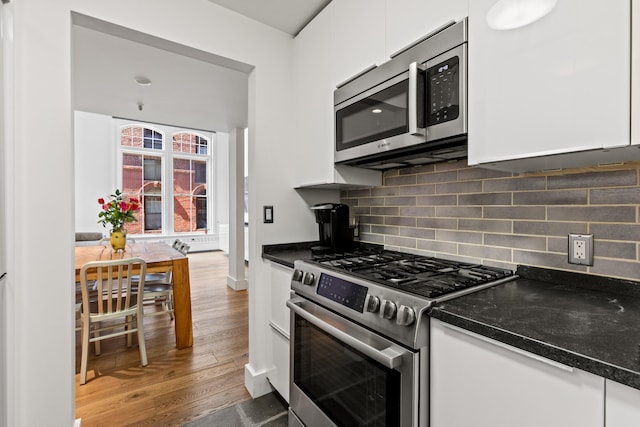 kitchen featuring stainless steel appliances, white cabinets, wood finished floors, tasteful backsplash, and baseboards