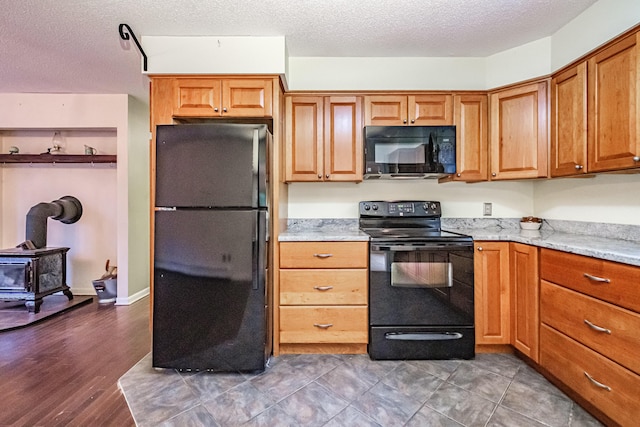 55 Reservoir Rd, Paris, ME 04281 - kitchen with black appliances, a wood stove, a textured ceiling, light stone counters, and brown cabinetry